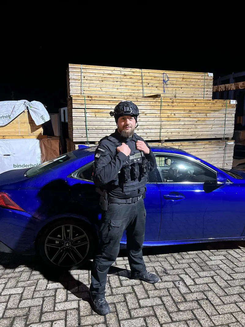 Sicherheitsmitarbeiter in Schutzausrüstung nachts vor gestapeltem Baumaterial